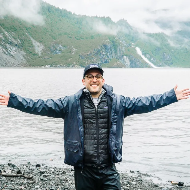 Travel advisor James Anello with his arms raised in front of a stunning mountain lake.