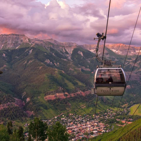 gondola going down a mountain with pink and purple skies, a great thing to do in the summer in Colorado