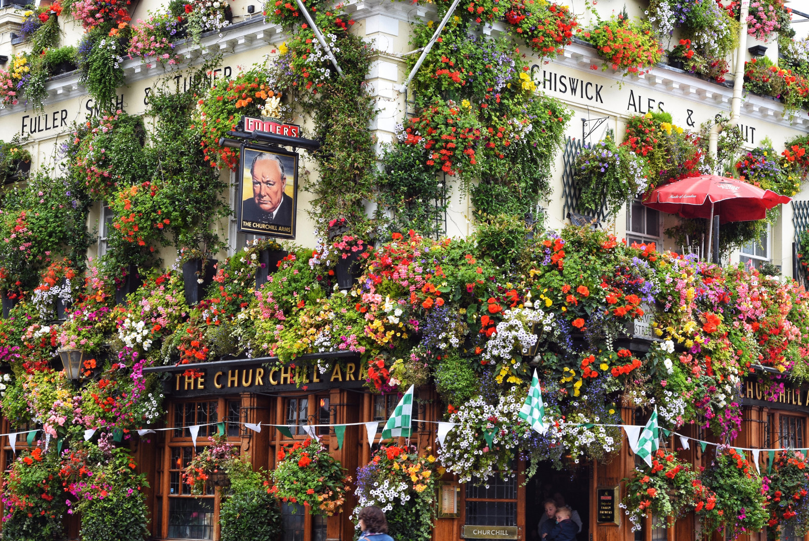 The Churchill Arms pub in London, England covered in green, pink, white and yellow flowers. 