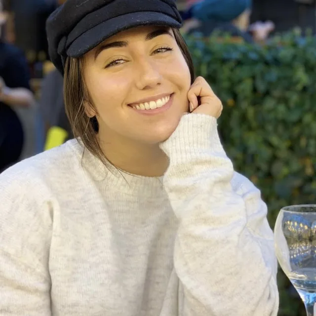 Fora travel agent Victoria Troost wearing black hat and tan sweater with green foliage