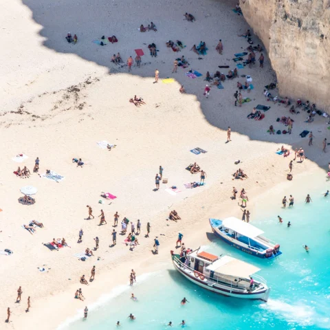 aerial view of people on a beach next to ocean and boats