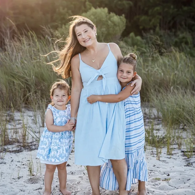 women wearing white dress standing next to two kids on sandy beach