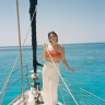 Fora travel agent wearing white pants standing on white boat with water in background on sunny day