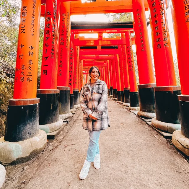 Travel Advisor Sierra ONeal with a plaid coat and jeans on standing in front of red Japanese archways.