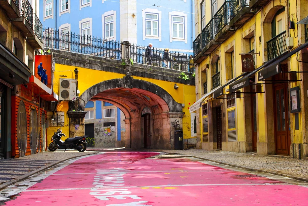 a pink street surrounded by yellow, baby blue, and red buildings