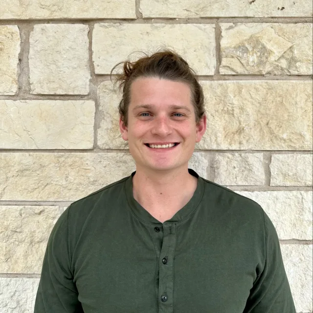 Travel Advisor Jordan Nocerino in a green shirt in front of a tan brick wall.