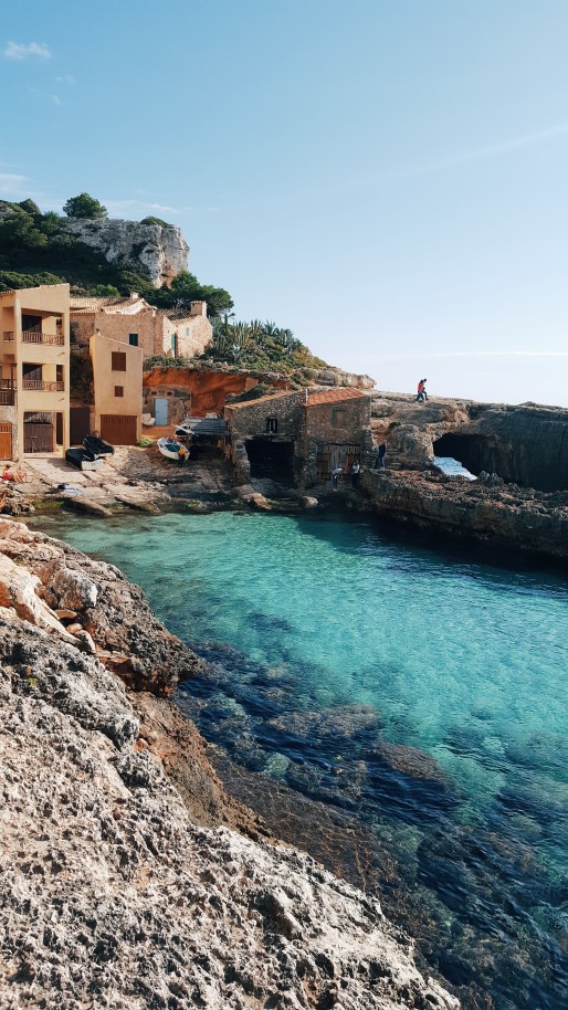 Tan buildings on top of seaside cliffs by serene turquoise waters in Mallorca, Spain. 