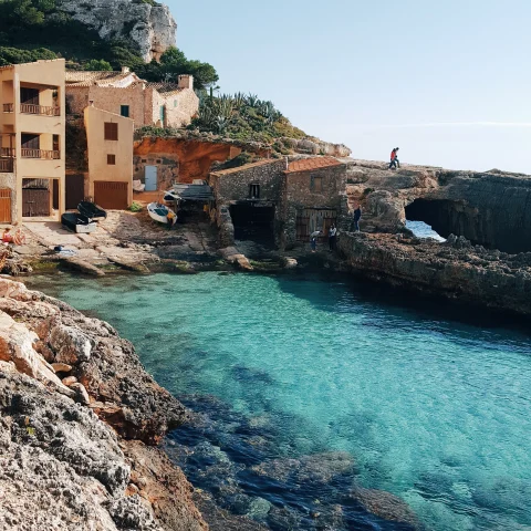 Tan buildings on top of seaside cliffs by serene turquoise waters in Mallorca, Spain. 