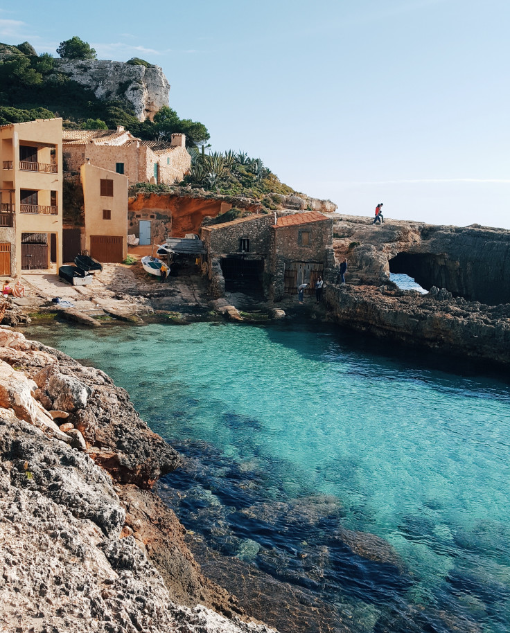 Tan buildings on top of seaside cliffs by serene turquoise waters in Mallorca, Spain. 