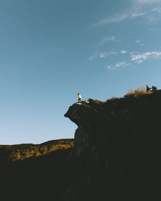 A person standing on the edge of the clifftop of Boone Mountain with blue sky overhead