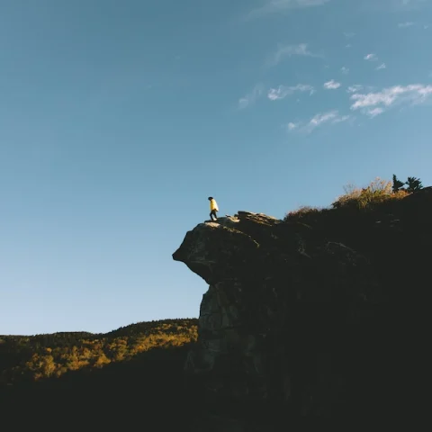 A person standing on the edge of the clifftop of Boone Mountain with blue sky overhead