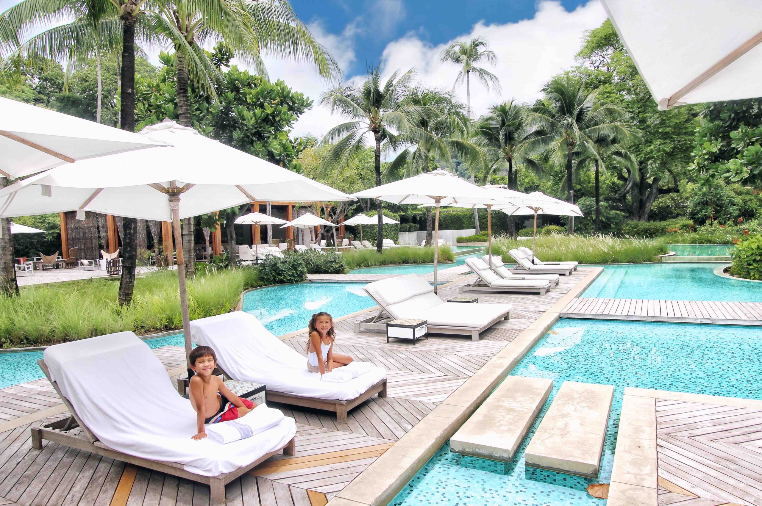 Phuket, two kids sitting on lounge chairs at the poolside.