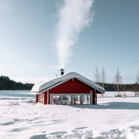 A picture of a red wooden house amongst snow in Finland.