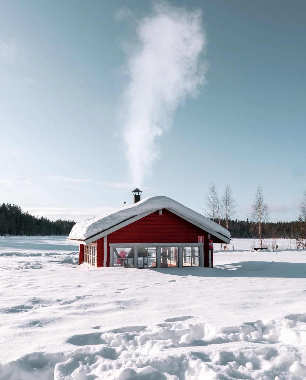 A picture of a red wooden house amongst snow in Finland.