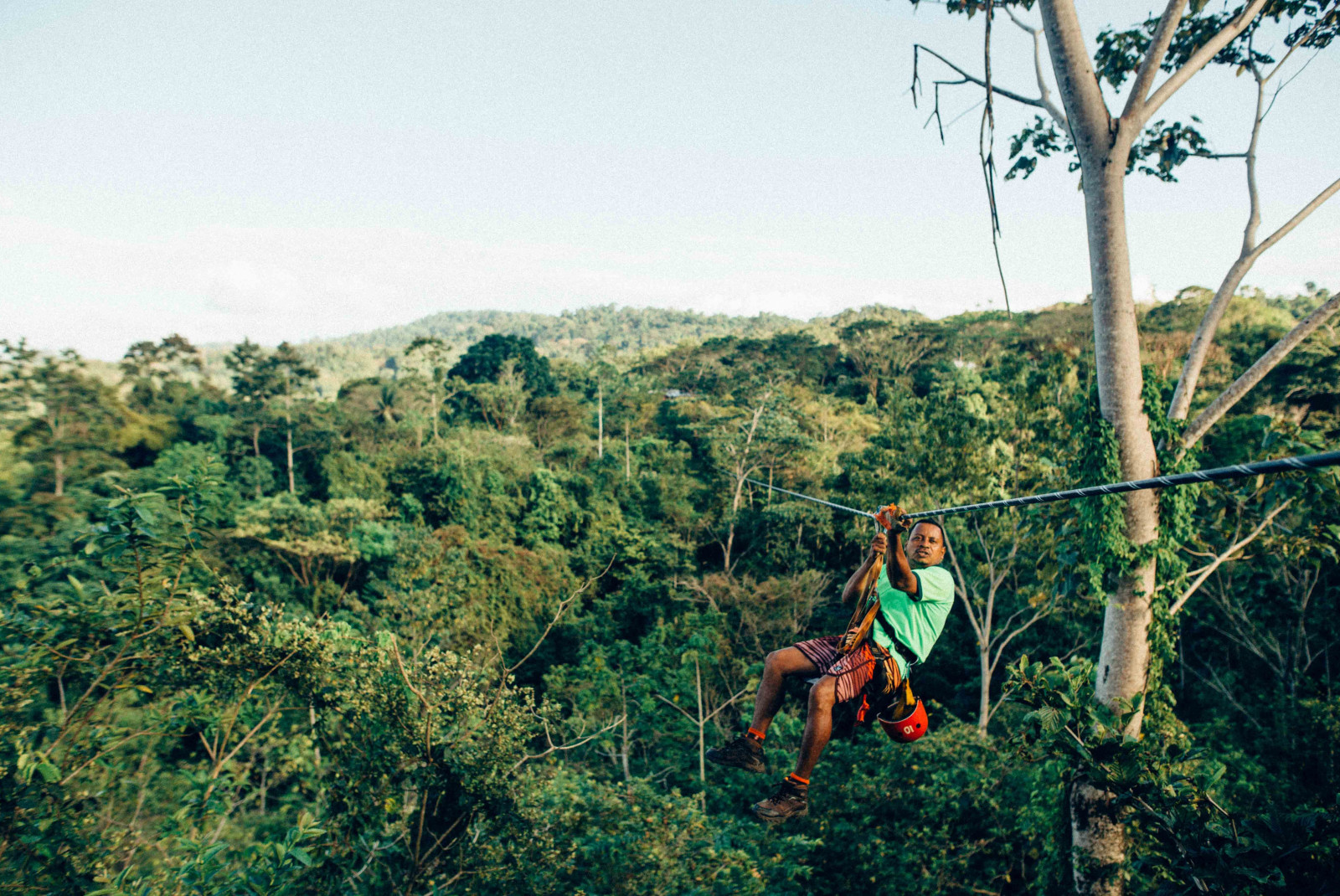 Man wearing green shirt hangs on zip line surrounded by trees in Costa Rica