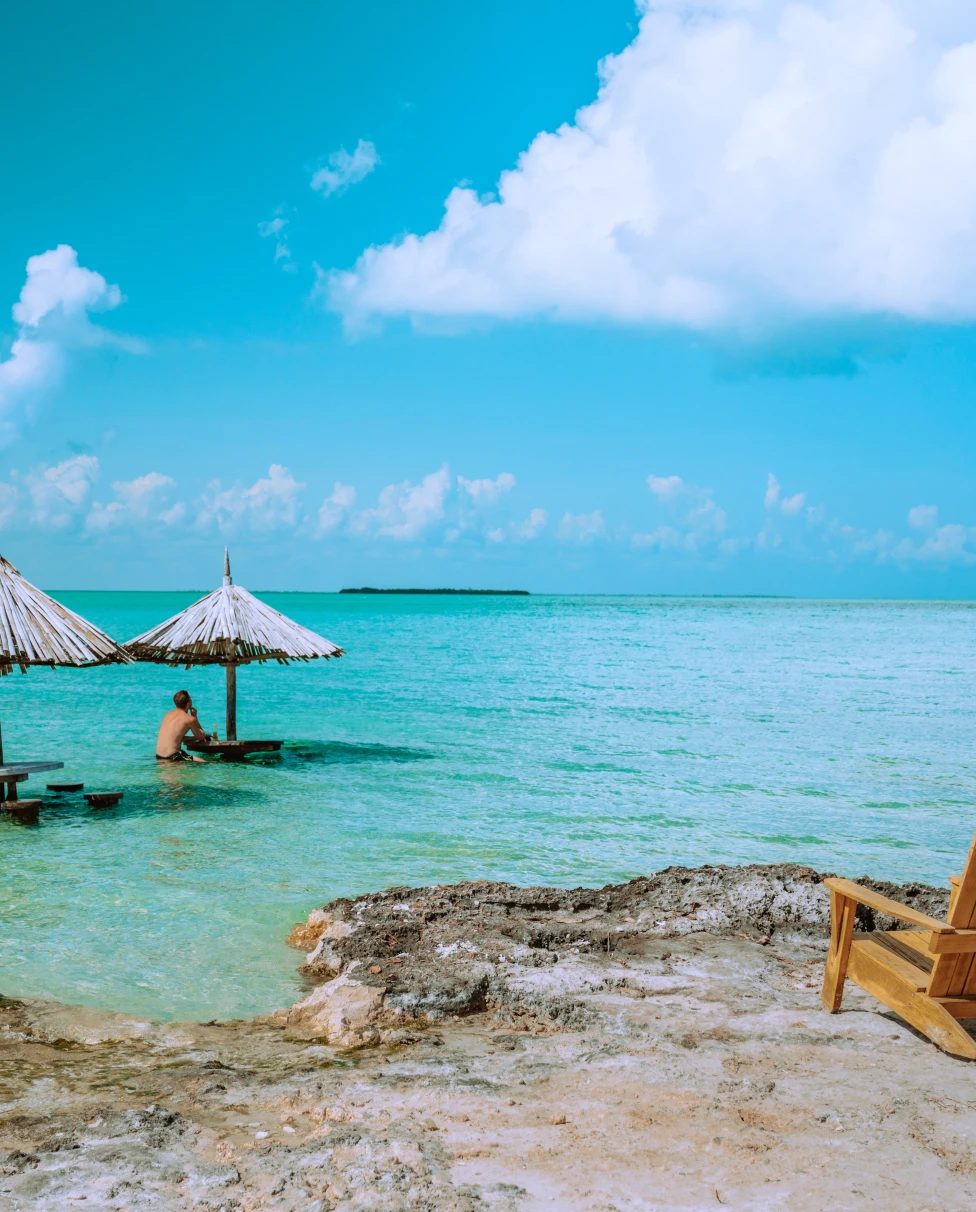 A beach view of Belize with wooden lounge chair and umbrella.