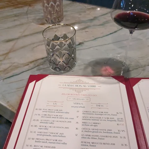 A wine menu and a glass of red wine on table.