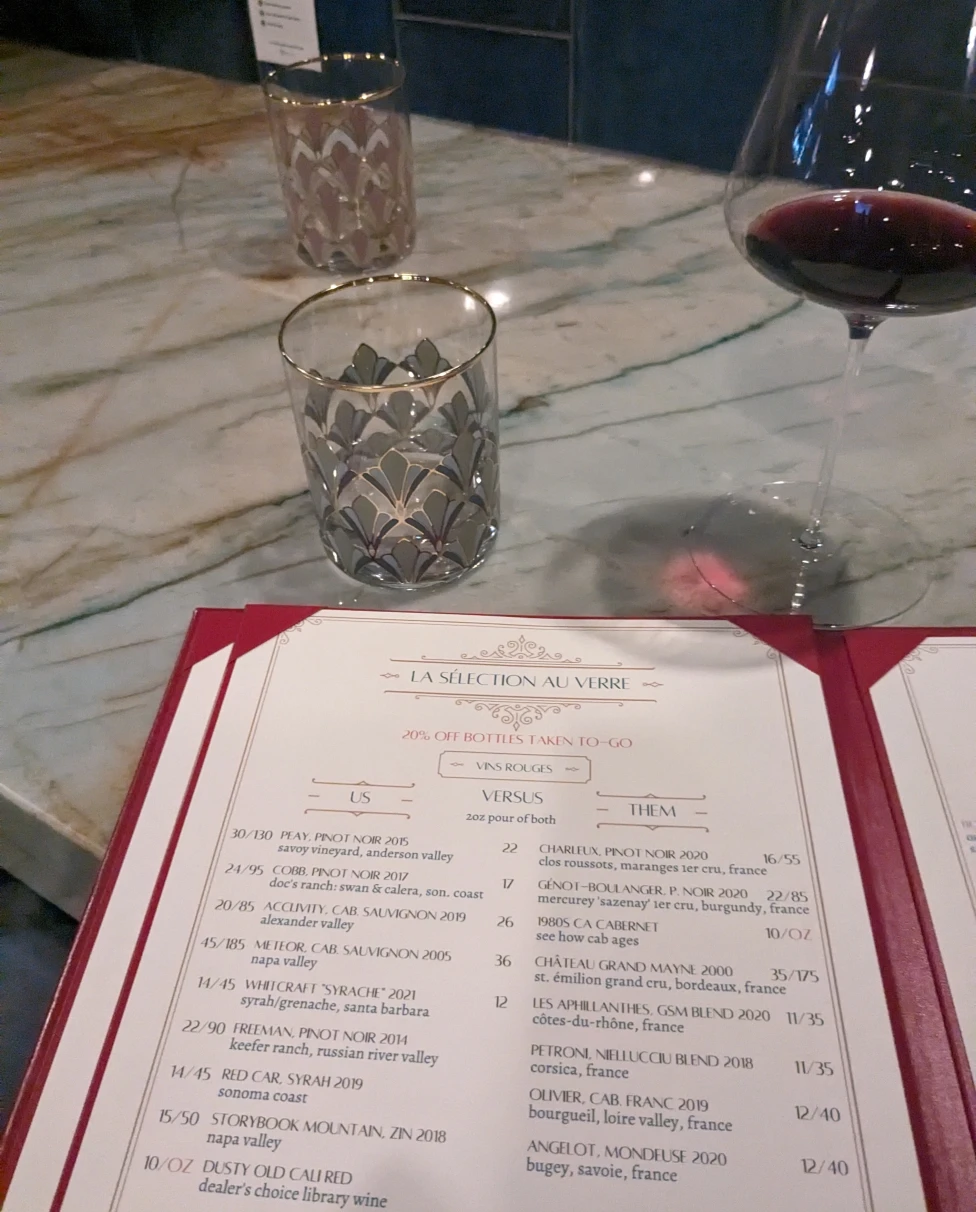 A wine menu and a glass of red wine on table.