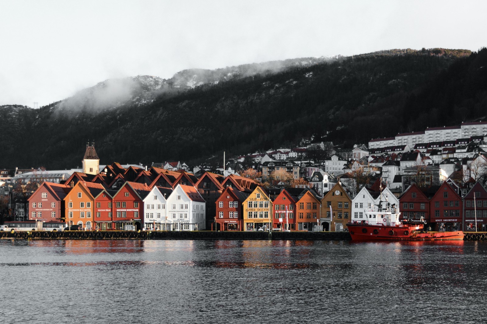 White red and yellow buildings next to body of water and mountain with cloudy skies