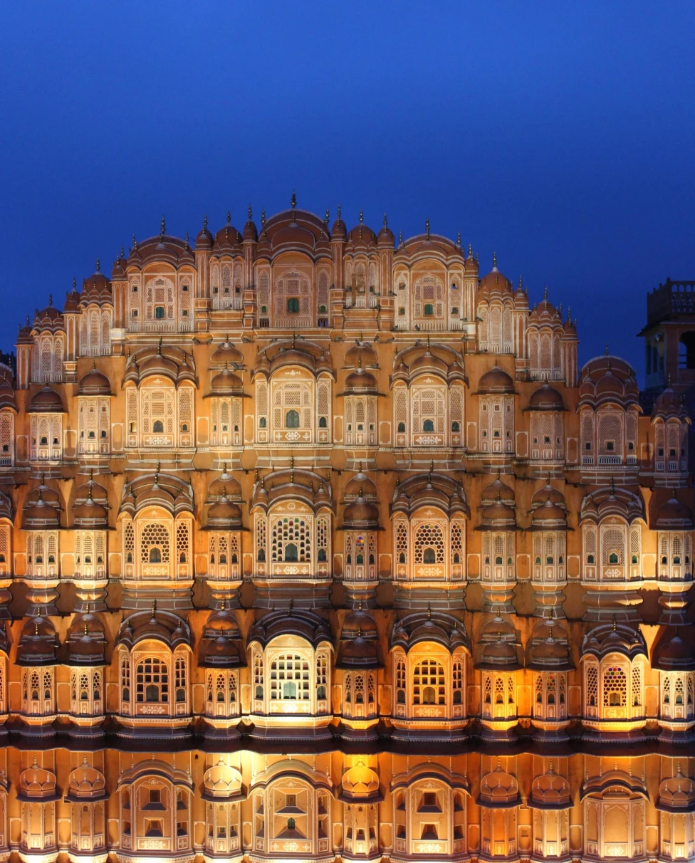 a tiered building lit up at night with a bright blue sky at night above