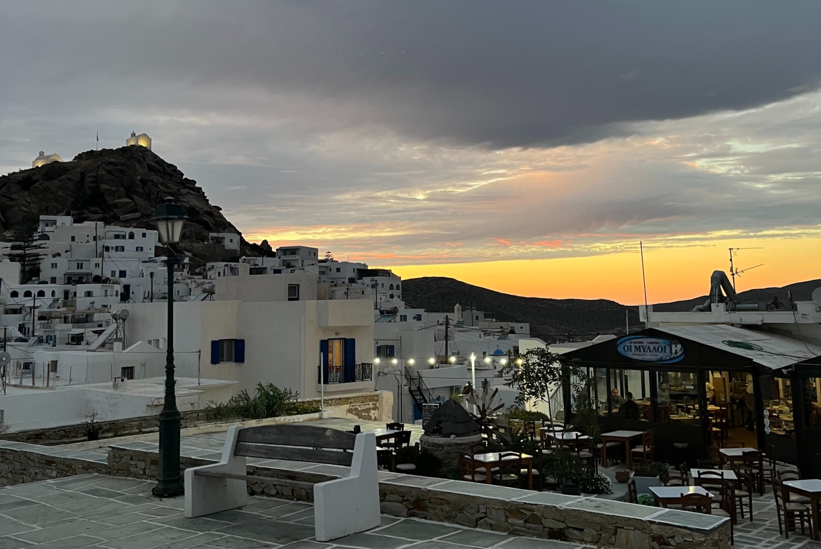 Sunset in cloudy sky from island town with white stone buildings in Ios, Greece.
