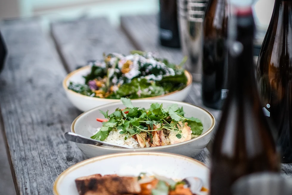 Three white bowls of food on a wood table with bottles of water