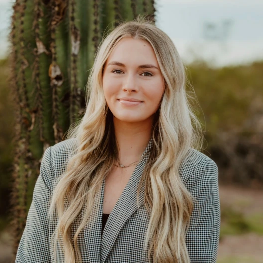 Travel Advisor Kaili Fuller in white and black checkered blazer in front of a cactus. 