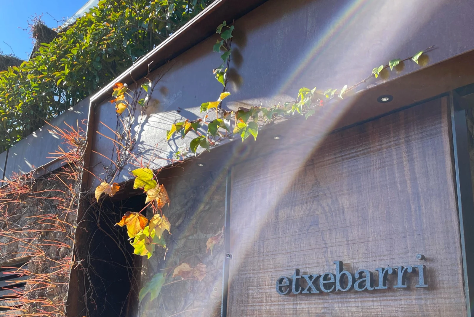 sun beam shines down over a wooden door entrance to a restaurant that reads, "etxebarri."