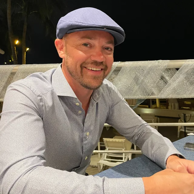 Travel advisor Chris Schille smiling at a table wearing a dress shirt and hat.