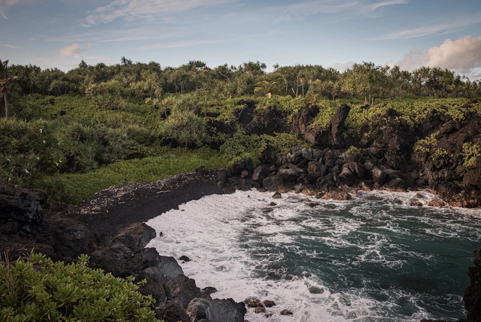 Cove with lush greenery and black sands in Keawaiki Bay, Hawaii.