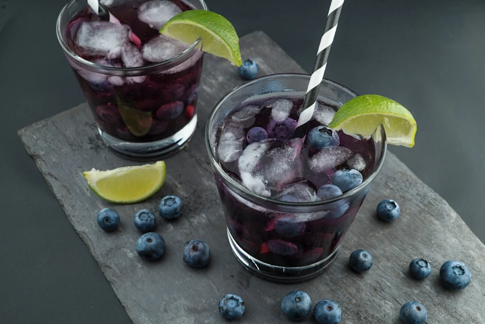 Two glasses of blue berry juice with ice and lemon.