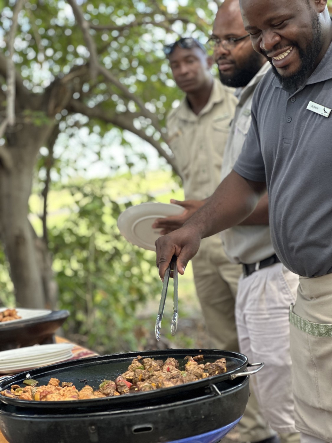 Three guides barbecuing lunch on an outdoor table with trees in the background