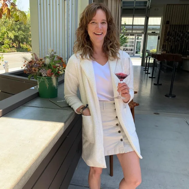 Travel advisor Deanna Basham posing in a white dress with a wine glass in hand.