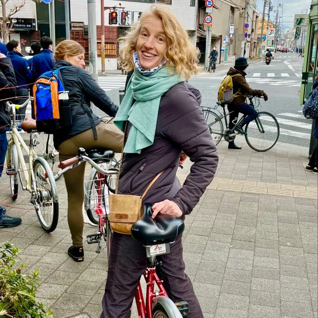 Travel Advisor Michelle Millerd on a red bicycle wearing a turquoise scarf and a brown cross body. 