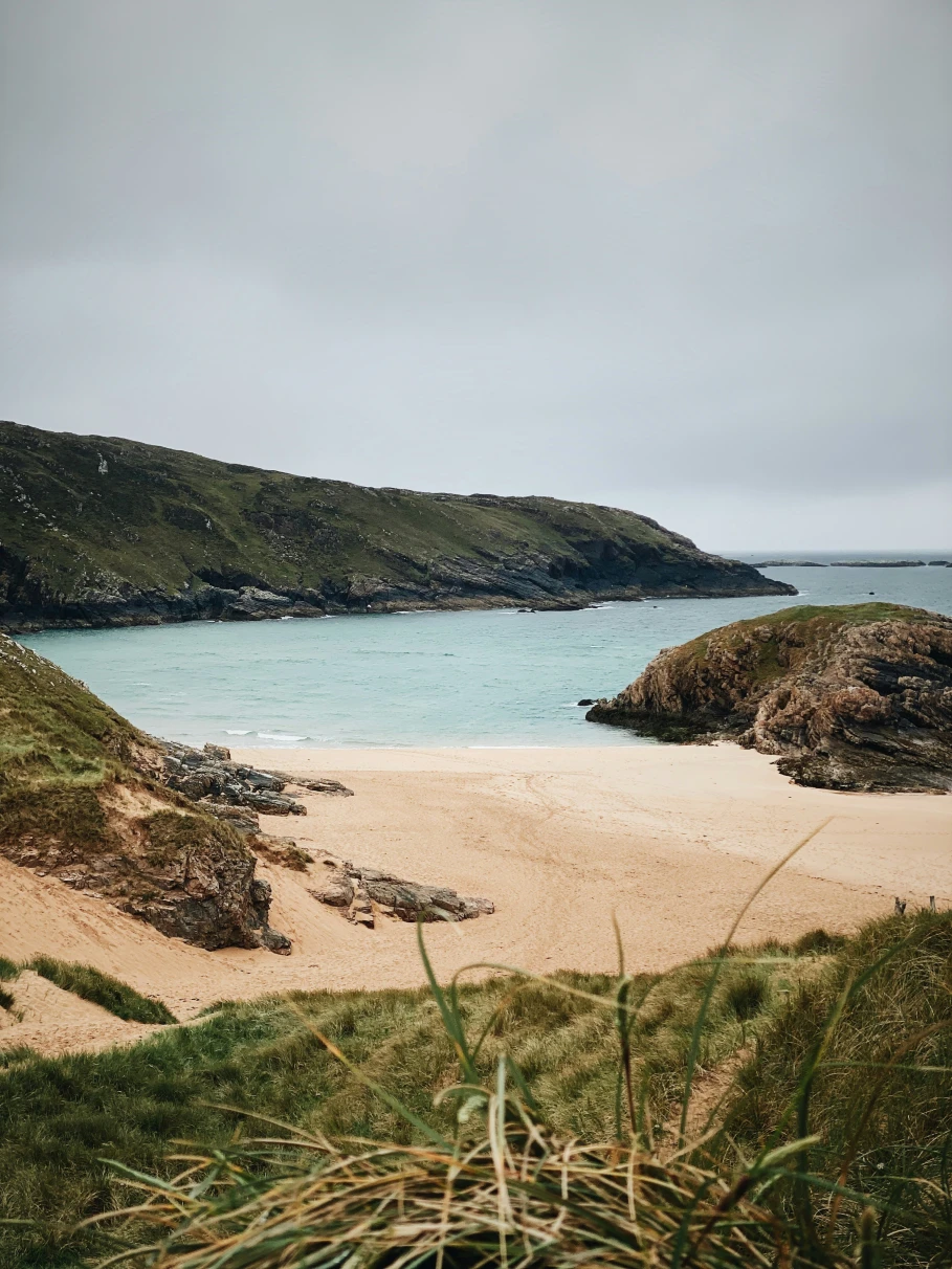 A sandy beach next to rock formations on a cloudy day at one of the Ireland beaches in Donegal.