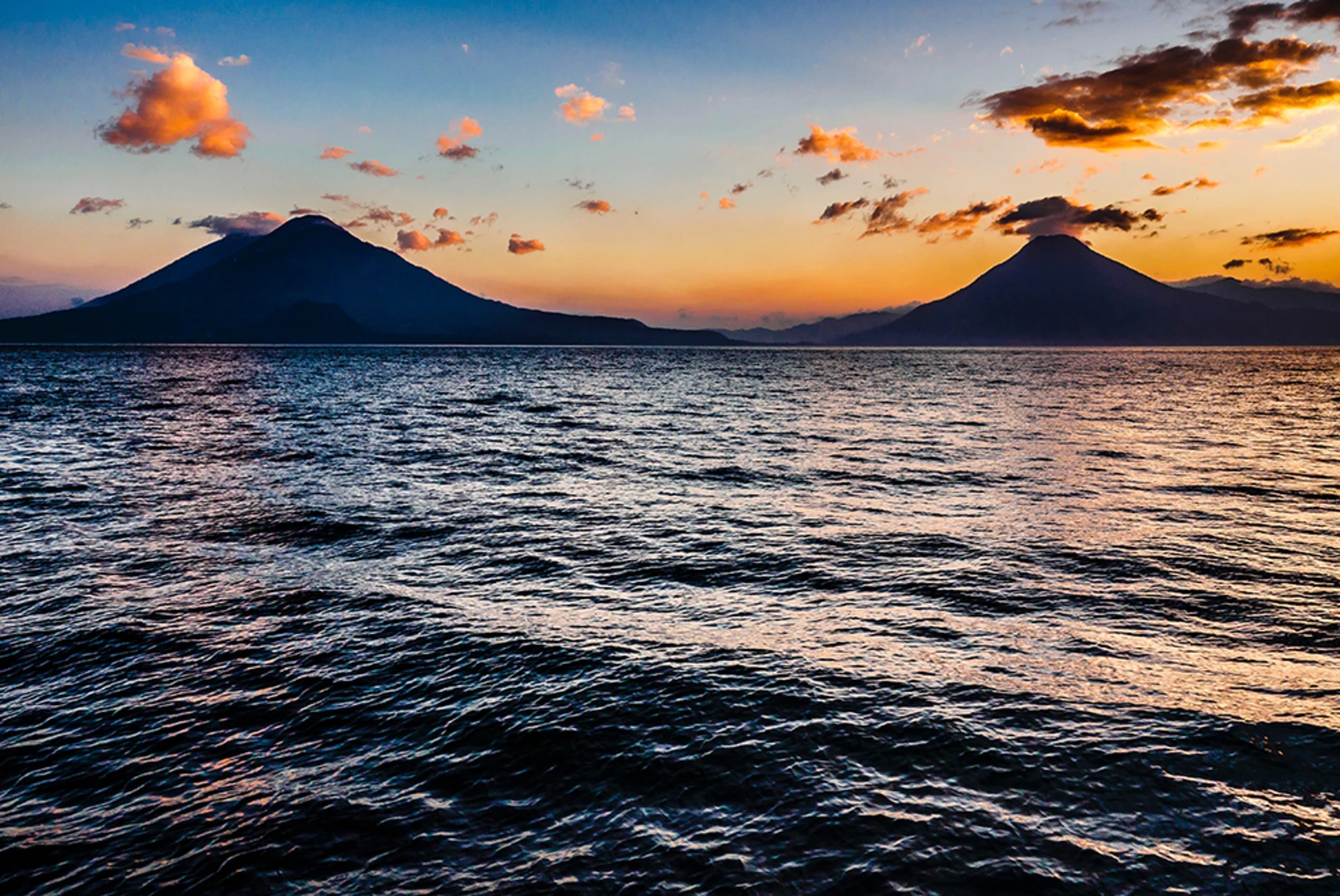 blue ocean at sunset in Guatemala with volcano mountains and pink clouds