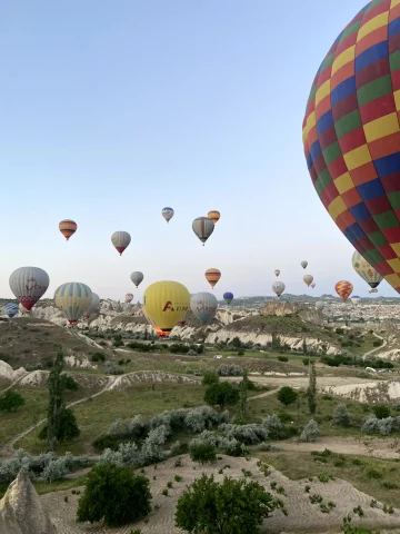 The image captures a picturesque scene of multiple colorful hot air balloons soaring over a rugged terrain under a clear blue sky. 