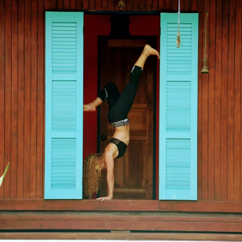 A yogi doing a headstand next to a blue door in Costa Rica. 