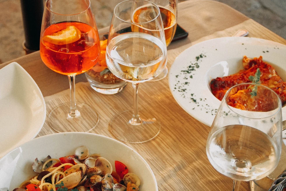 White bowls of pasta and glasses of wine on wooden table
