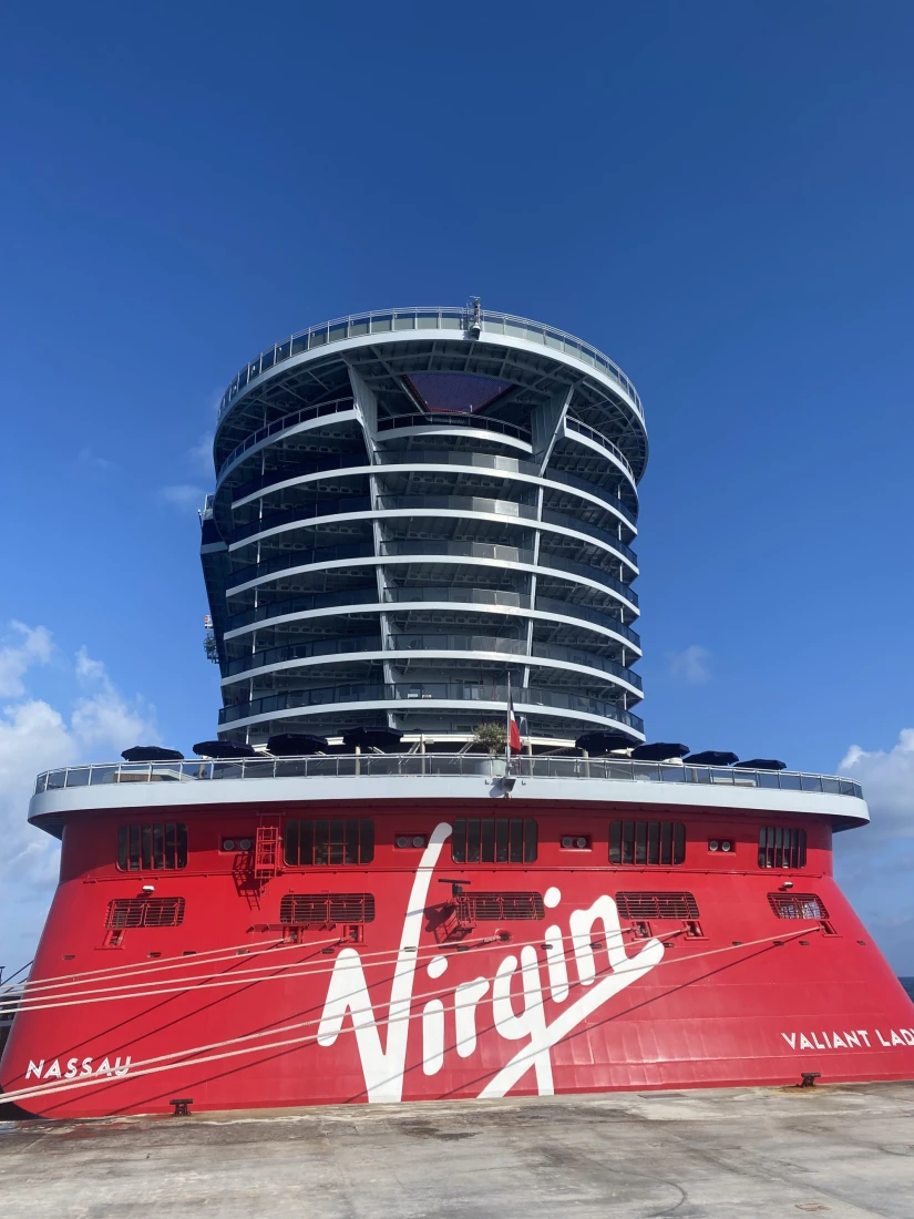 A view of the top of the cruise ship with a round set of balconies and a red painted exterior that reads "Virgin" in white lettering. 
