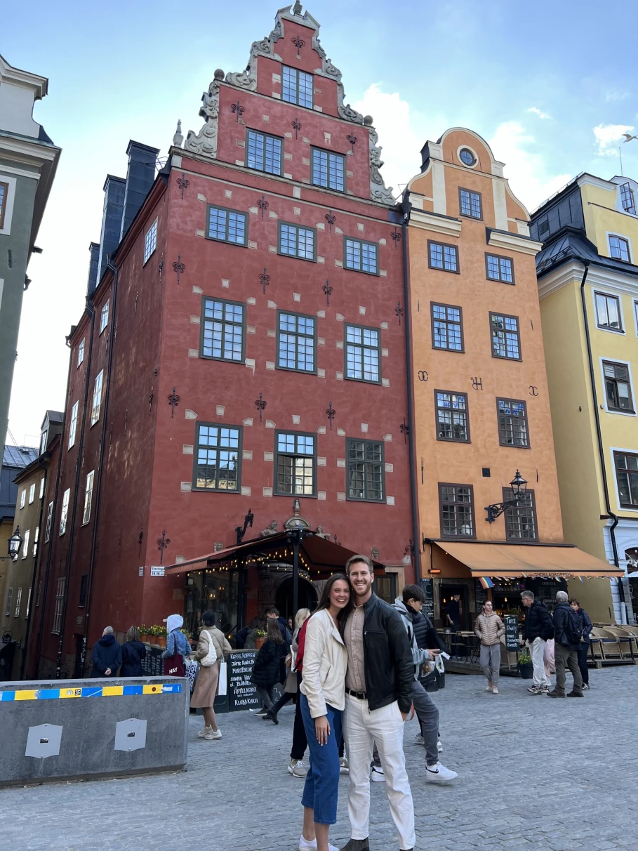 A couple smiling and posing in front of colorful buildings in Stockholm's Old Town.