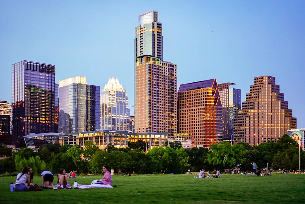 people sitting on the grass in the park with a modern cityscape in the afternoon