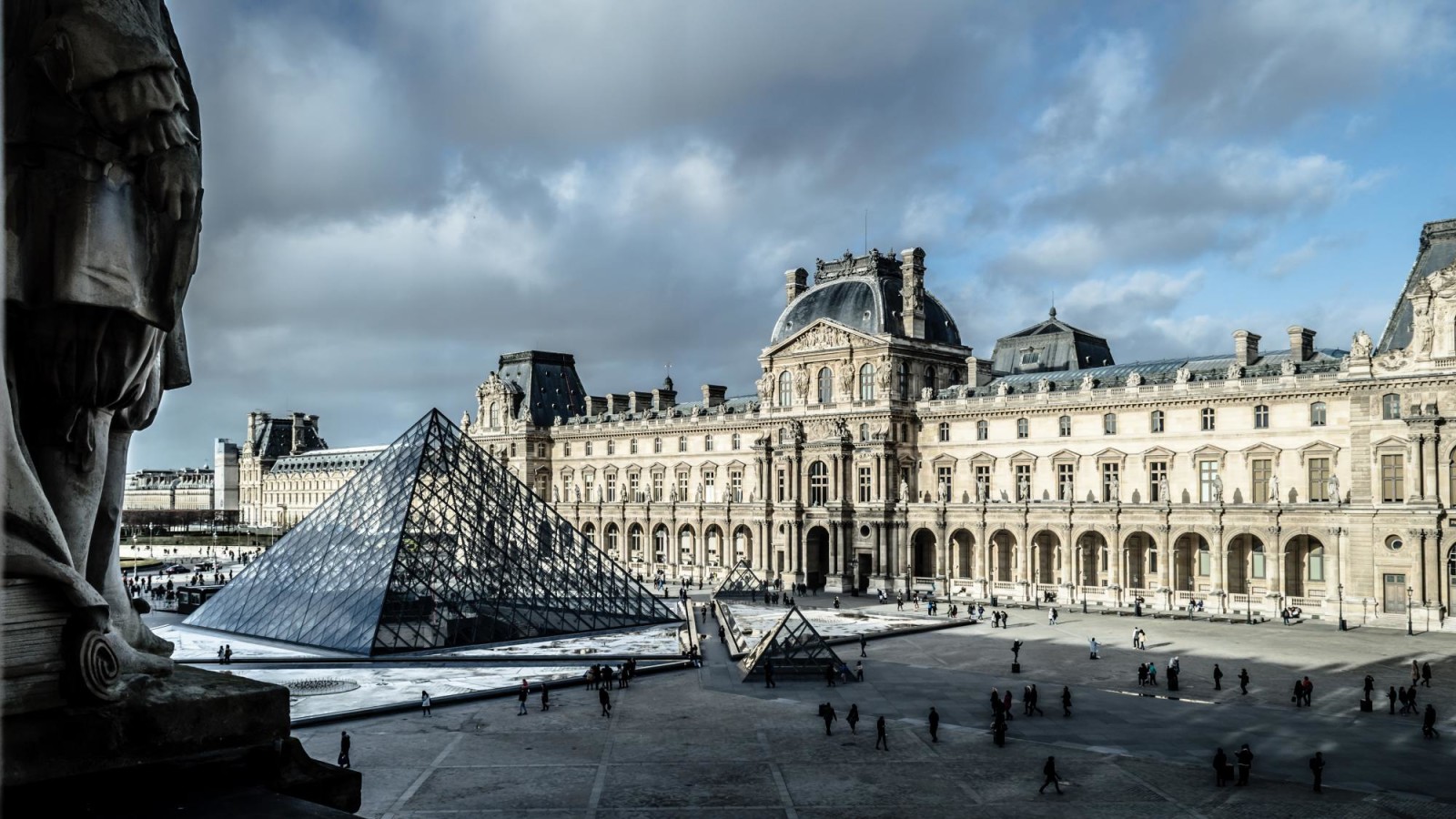 The entrance of the Louvre and famous pyramid in Paris on a cloudy day.