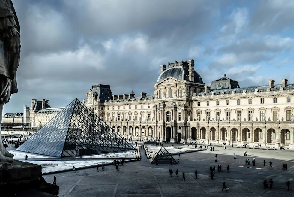 The entrance of the Louvre and famous pyramid in Paris on a cloudy day.