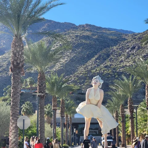 Statue of Marilyn Monroe between palm trees and in front of mountains. 