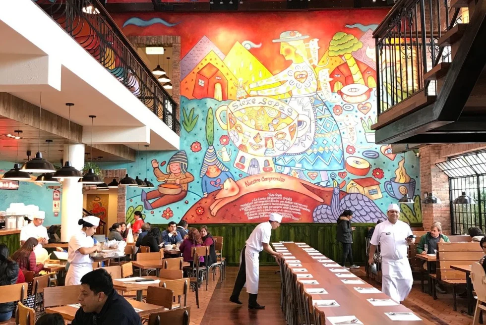 A restaurant with waiters dressed in white and a colorful big painted wall.