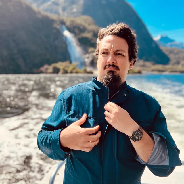 Travel Advisor Ramses Perez wearing a green shirt in front of mountains and a waterfall.