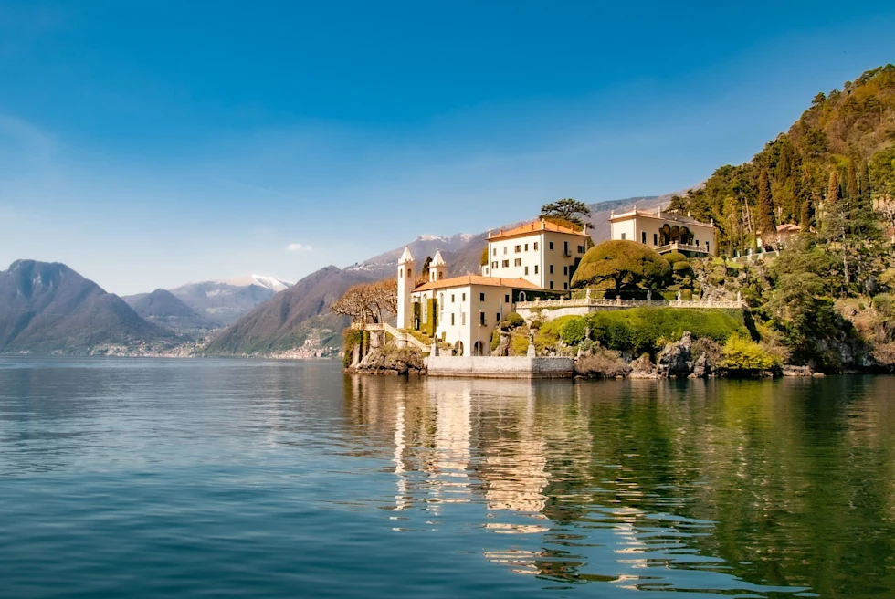 Lake with a white and orange building and mountains around it.