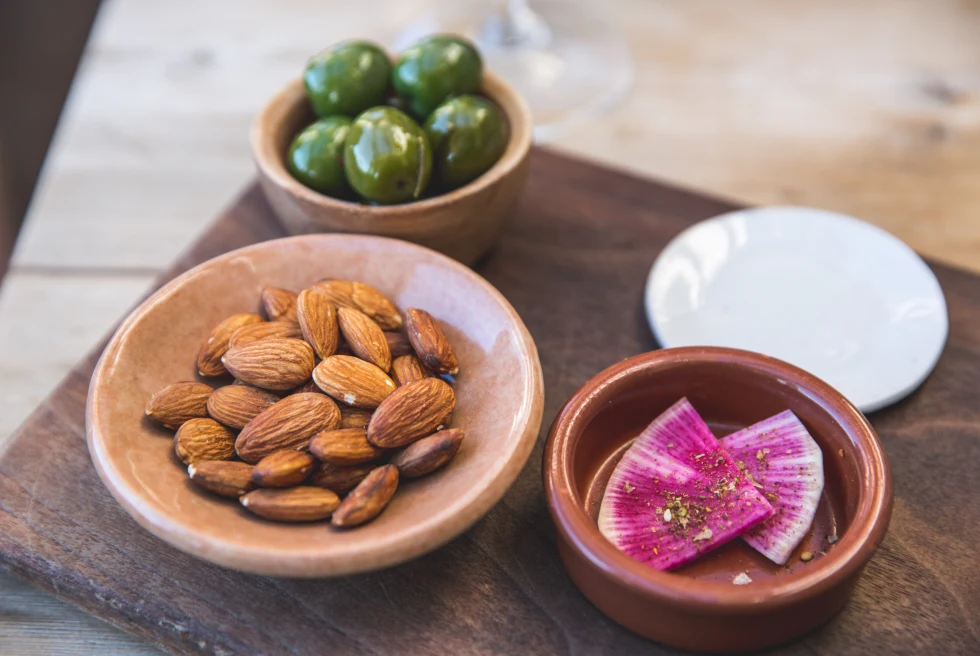 Almonds, olives, and radishes in bowls served on a wooden platter
