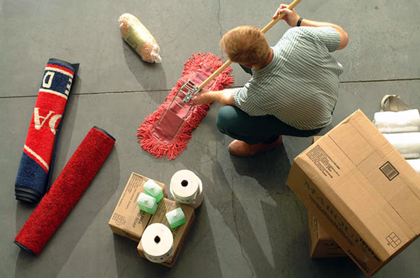 Man dry mopping a floor with mats.